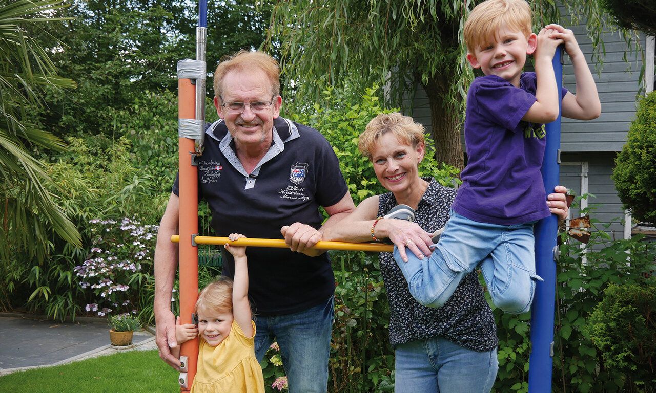 Großeltern stehen mit zwei Enkelkindern im Garten an einem Klettergerät