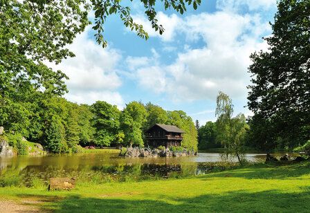 Bäume, Wiese und ein Holzhaus auf einem See im Sommer