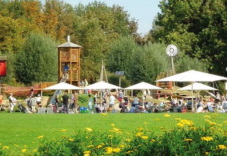 Wiese, Blumen und Bäume und ein Spielplatz mit großen Sonnenschirmen