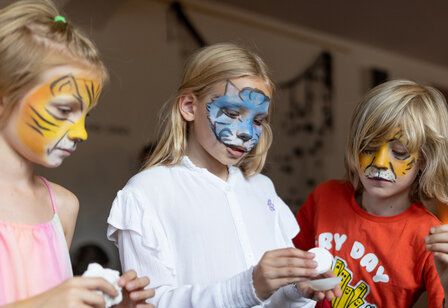 drei geschminkte Kinder basteln in den Räumen des Opernhauses