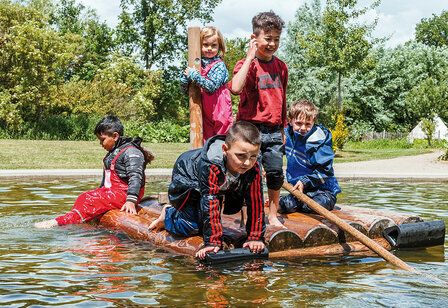 Kinder stehen auf einem Floß in einem kleinen Teich