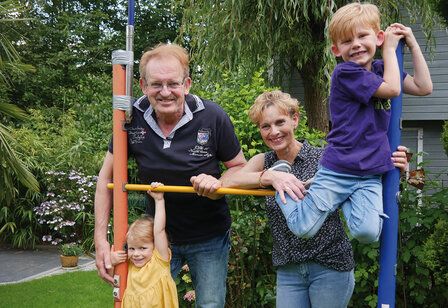 Großeltern stehen mit zwei Enkelkindern im Garten an einem Klettergerät