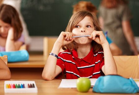 Ein Junge sitzt im Klassenzimmer an seinem Tisch und hält sich einen Bleistift vor den Mund