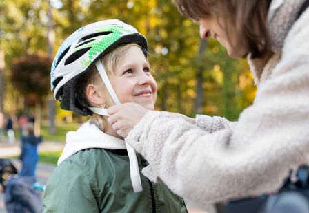 eine Mutter zieht ihrer Tochter einen Fahrradhelm auf, beide lächeln sich an