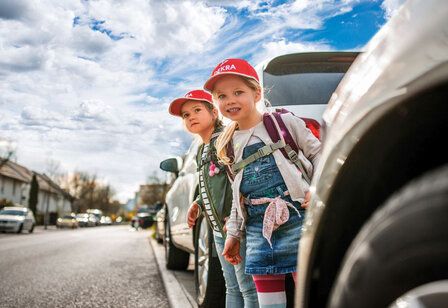 Zwei Kinder stehen zwischen parkenden Autos und wollen die Straße überqueren