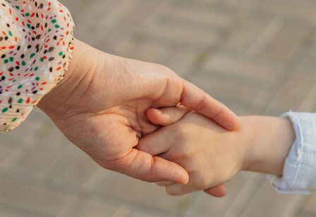 Die Hand einer Frau hält die Hand eines Kindes, im Hintergrund Pflastersteine