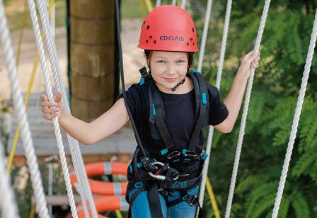 Mädchen mit Helm klettert im Hochseilgarten