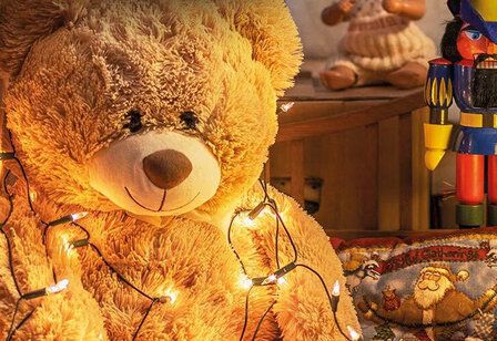 Teddybär mit Lichterkette umgehängt, im Hintergrund ein Nussknacker