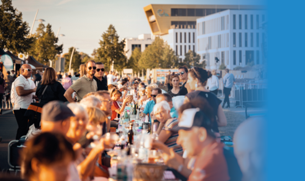 Lange Tafel auf der Strasse mit vielen Menschen die gemeinsam essen, trinken und sich unterhalten 