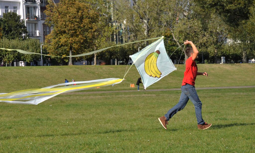 Kind läuft mit einem Drachen auf der Rheinwiese