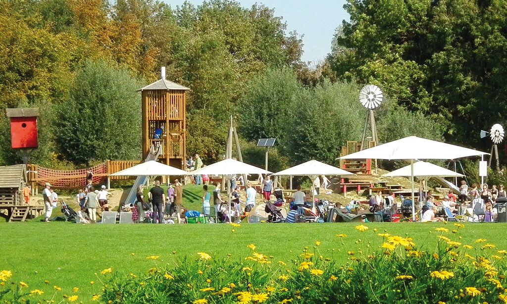 Wiese, Blumen und Bäume und ein Spielplatz mit großen Sonnenschirmen