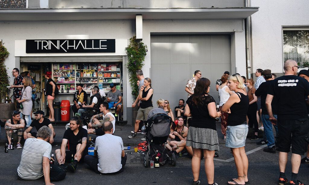 Viele Leute stehen und sitzen entspannt vor einer Trinkhalle