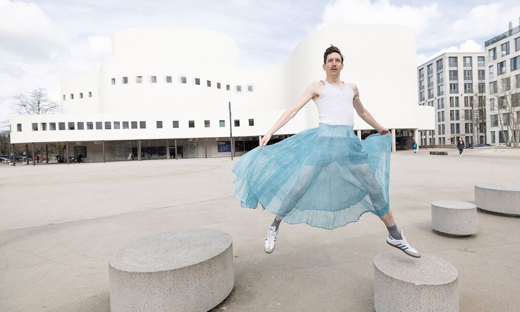 Schauspieler im hellblauen Tütü tanzt auf dem Gustaf Gründgens Platz vor dem Schauspielhaus