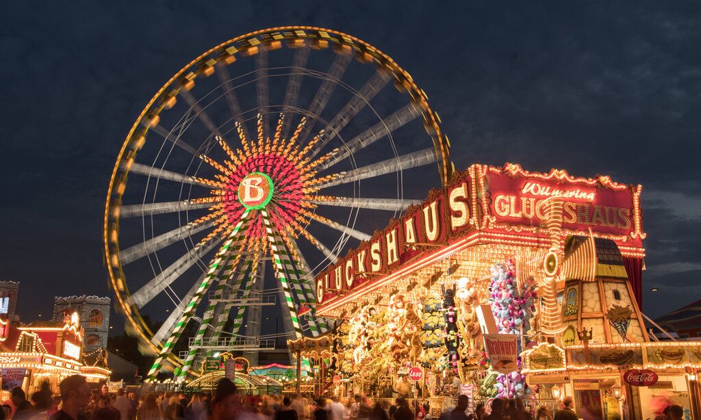 Das beleuchtete Riesenrad und das Glückshaus auf dem Düsseldorfer Kirmesplatz am Abend