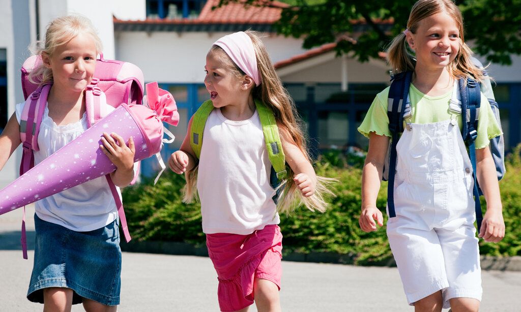 Drei Mädchen laufen nebeneinander her, das Mädchen links trägt eine Schultüte