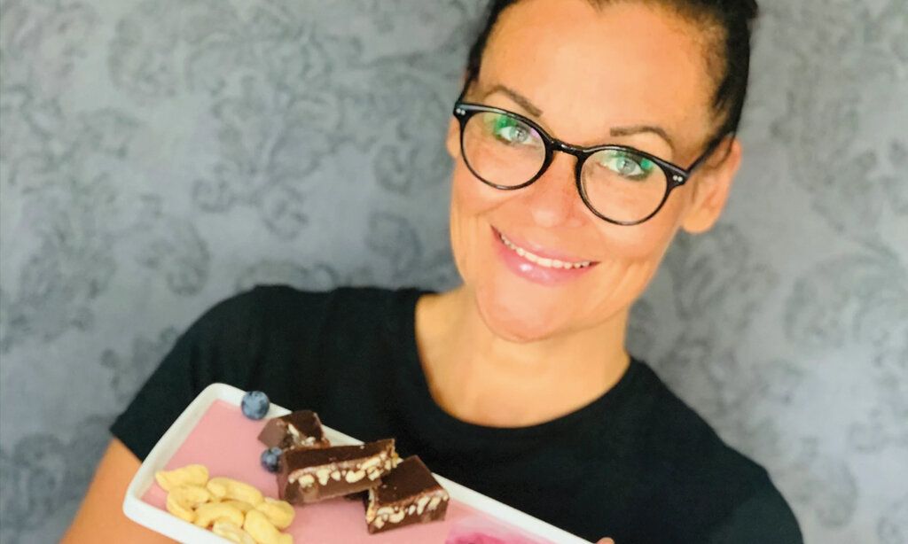 Porträt von Anja Hohmann, die einen eckigen Teller mit Schokolade, Cashewkernen und Blaubeeren hält