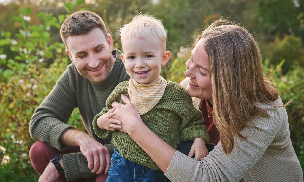 Vater, Mutter mit kleinem Jungen, im Hintergrund Gebüsch