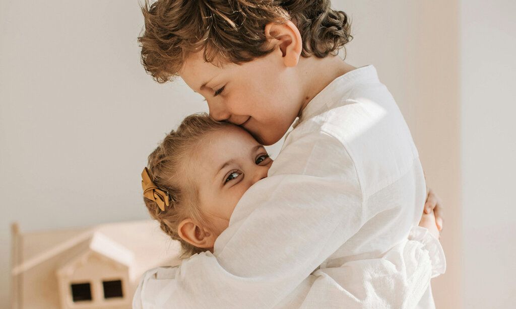 Geschwisterpaar umarmt sich, die kleine Schwester lacht in die Kamera, der große Bruder hat die Augen geschlossen