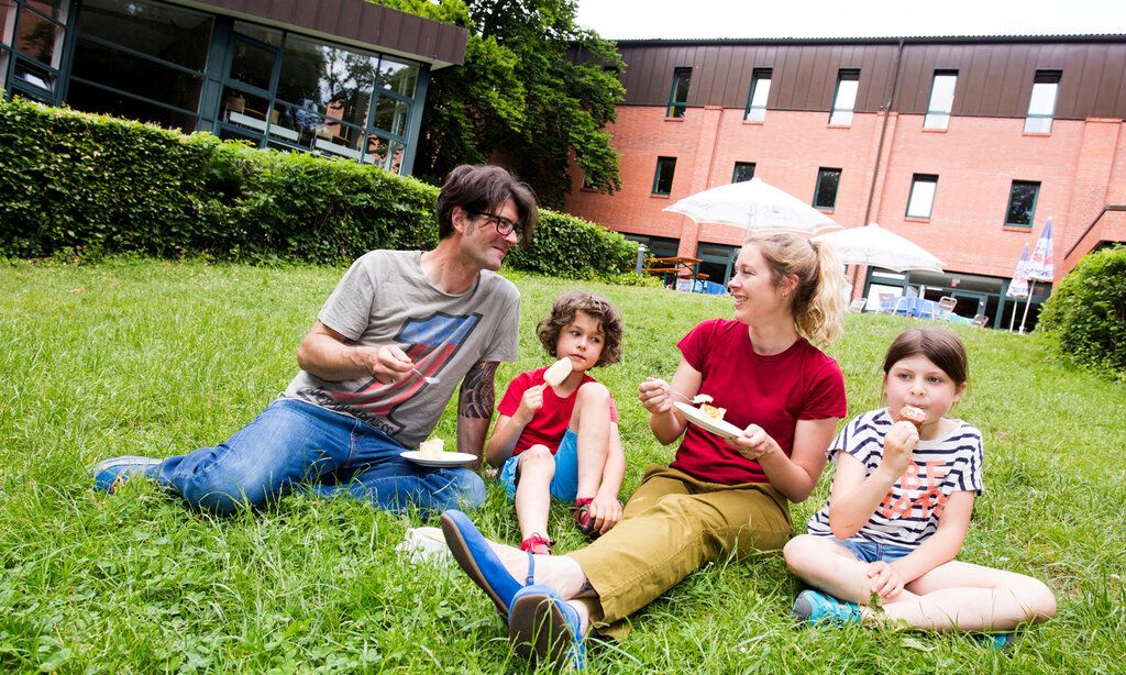 Vater, Mutter und zwei Kinder sitzen auf einem rasen vor der Jugendherberge in Bonn