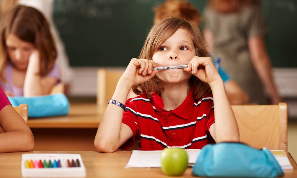 Ein Junge sitzt im Klassenzimmer an seinem Tisch und hält sich einen Bleistift vor den Mund