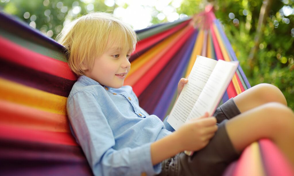 ein Junge liegt in einer bunt gestreiften Hängematte und liest ein Buch