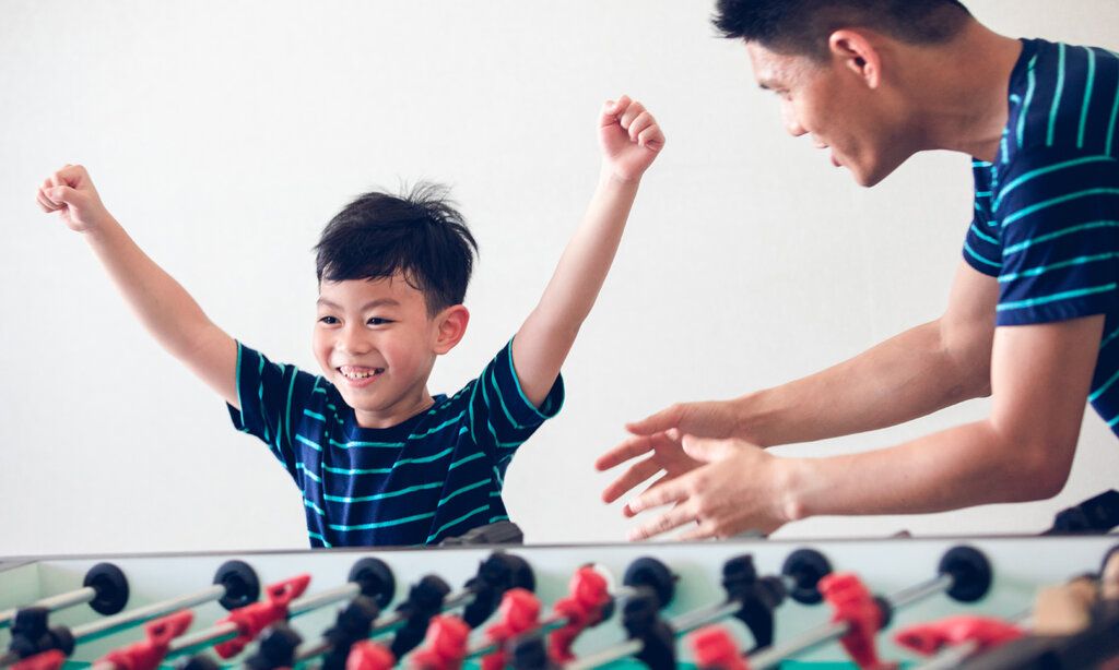 kleiner Junge steht mit seinem Vater an einem Tischfußball und jubelt