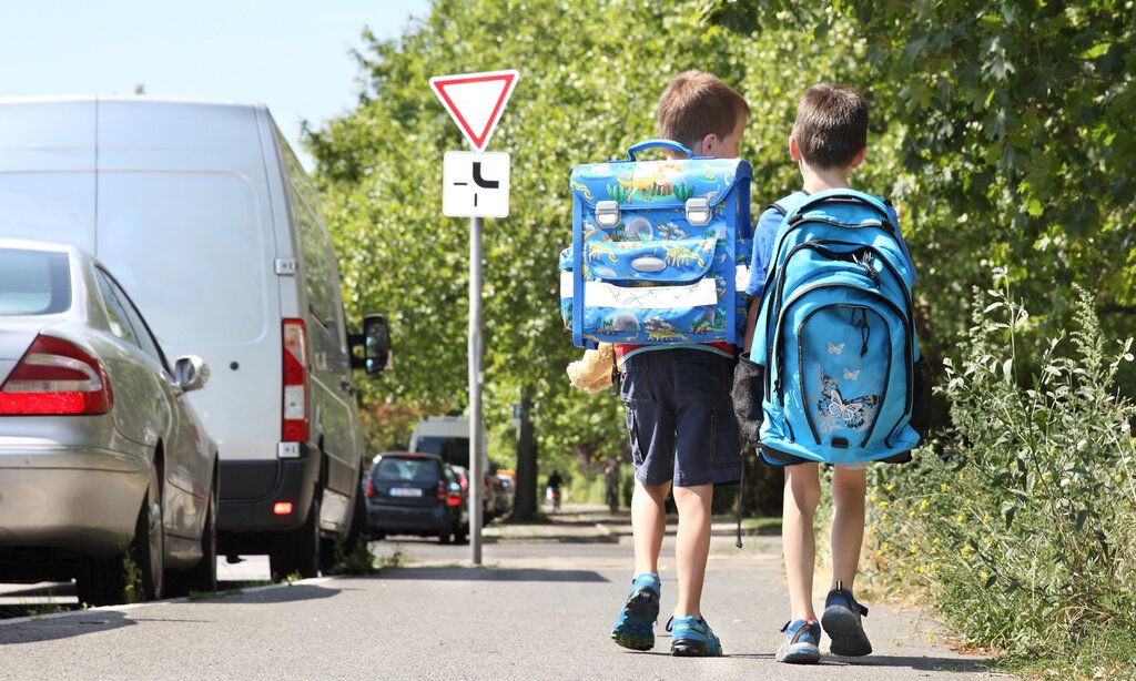 Zwei Jungs von hinten mit Schulrucksäcken gehen nebeneinander auf einem Bürgersteig