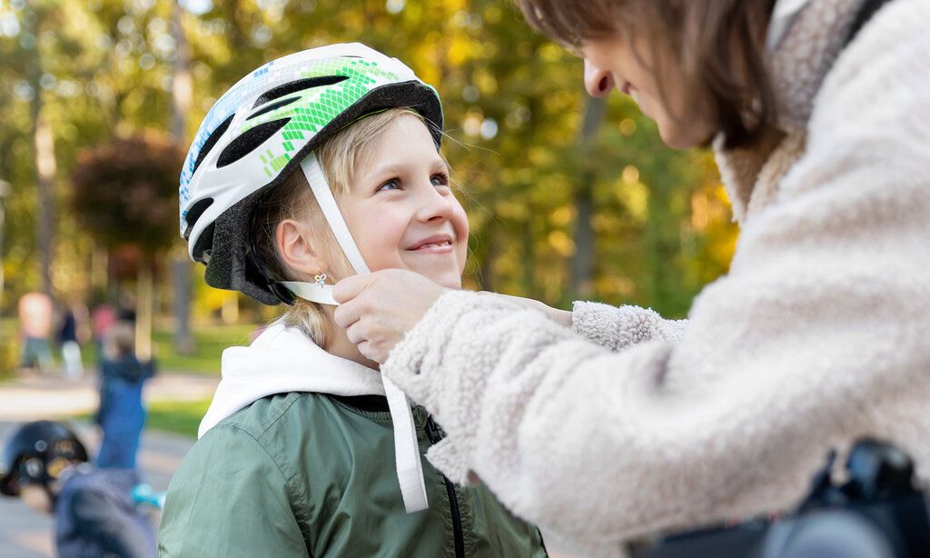 eine Mutter zieht ihrer Tochter einen Fahrradhelm auf, beide lächeln sich an