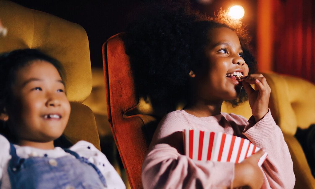 zwei Kinder sitzen im Kinosaal, ein Mädchen isst Popcorn