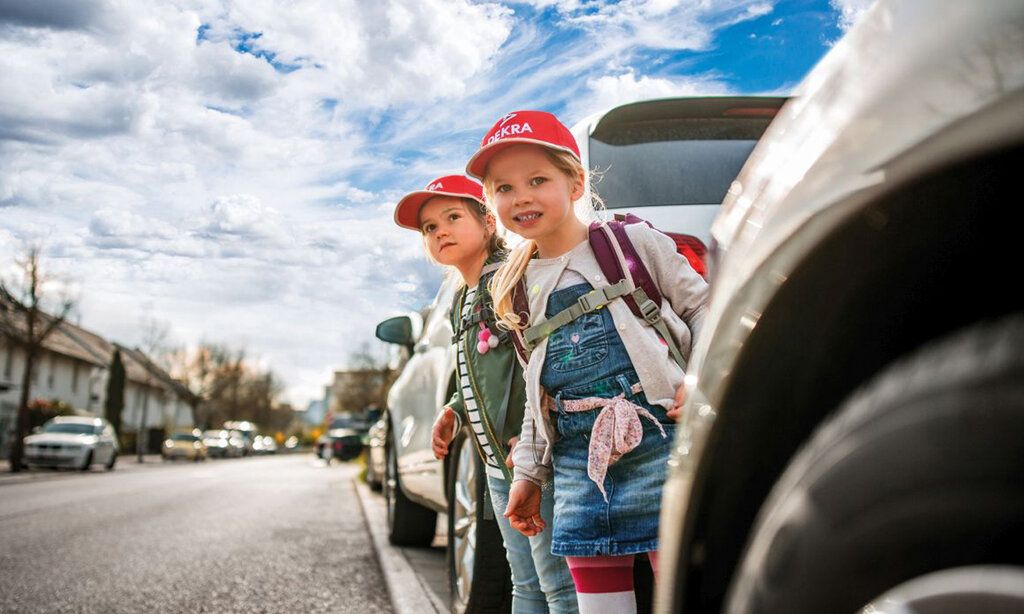 Zwei Kinder stehen zwischen parkenden Autos und wollen die Straße überqueren