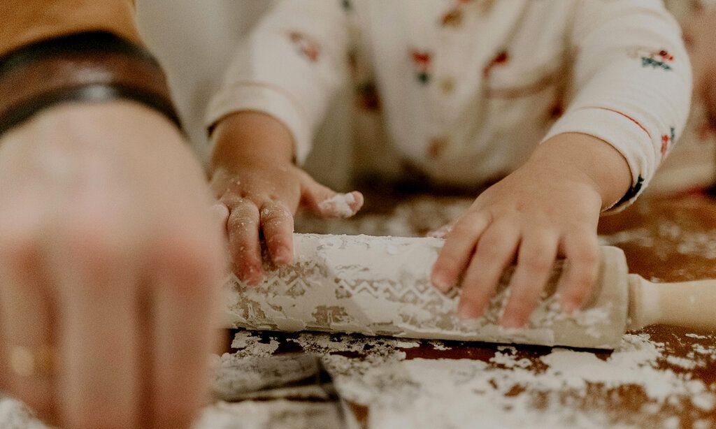 Detailaufnahme von Kinderhänden, die ein bemehltes Nudelholz anfassen