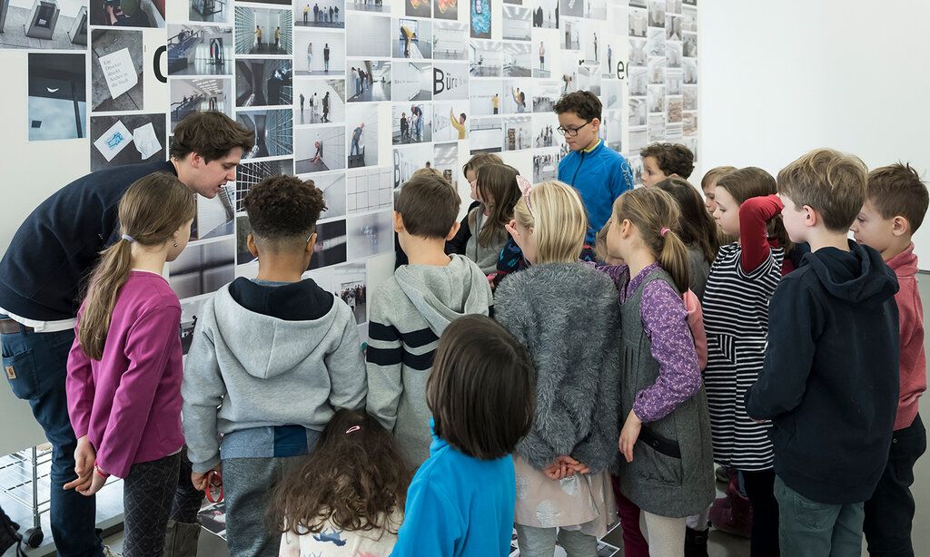 Museumspädagoge steht mit Kindern vor einem Kunstwerk und spricht mit ihnen darüber