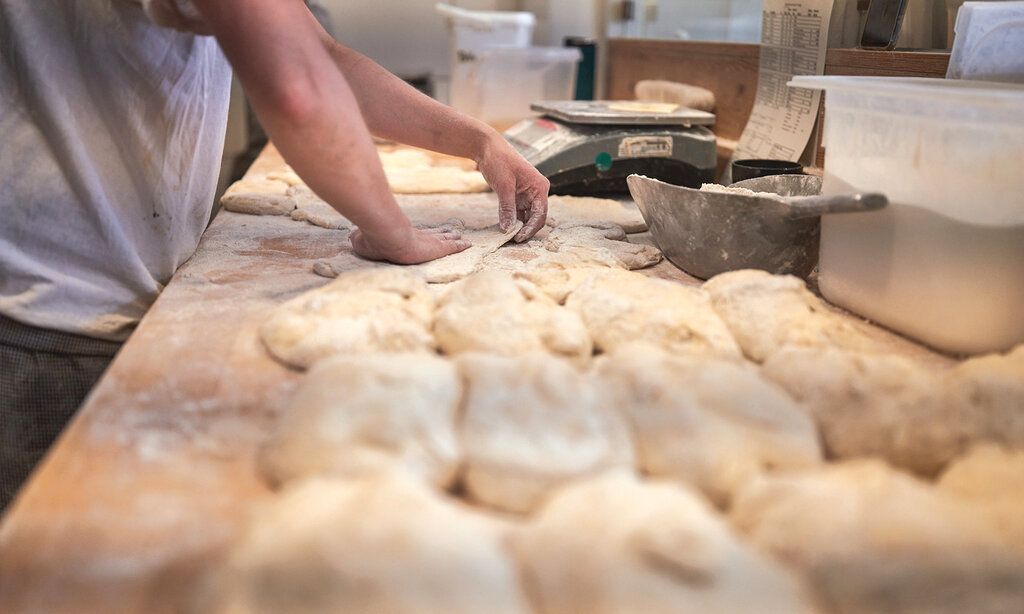 Ein Bäcker formt Brötchen aus Teig, man sieht nur die Arbeitsfläche, seine Arme und den Teig