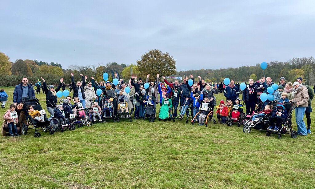 Familien mit Kindern in Rollstühlen stehen im Halbkreis auf einer Wiese, sie haben teilweis eblaue Luftballons in der Hand