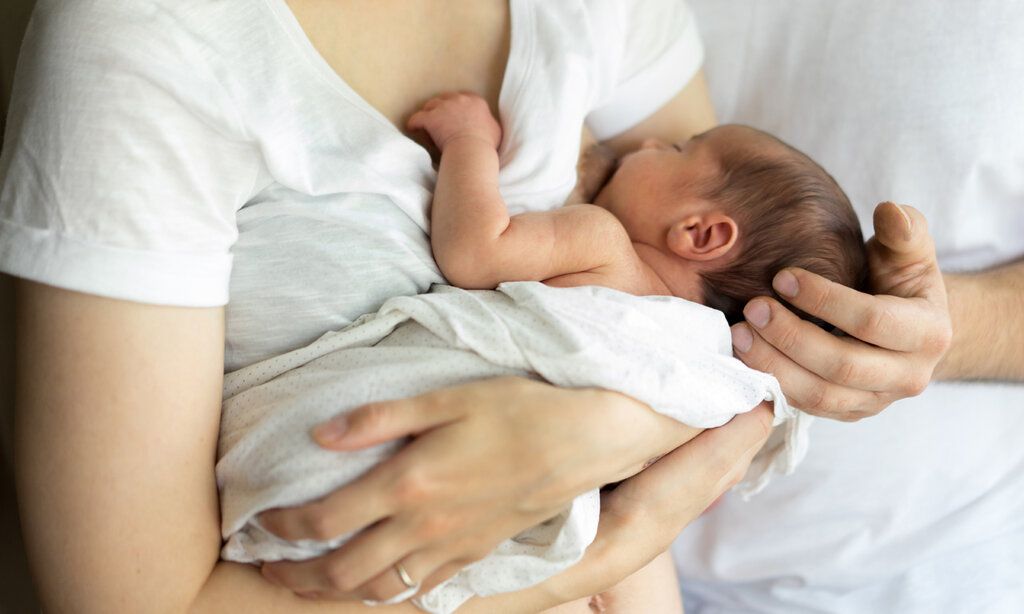 Mutter stillt Baby, Hand des Vaters hält den Kopf des Babys