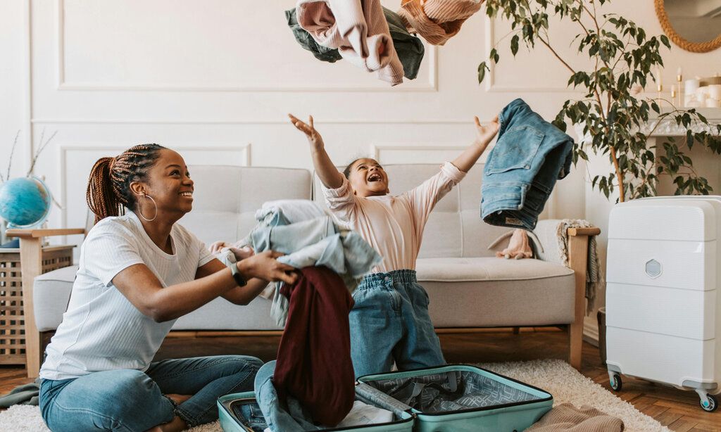 Mutter und Kind packen Koffer, das Kind schmeißt Anziehsachen in die Luft