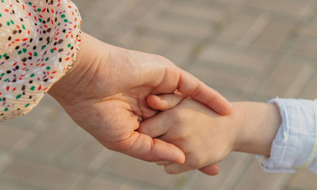 Die Hand einer Frau hält die Hand eines Kindes, im Hintergrund Pflastersteine