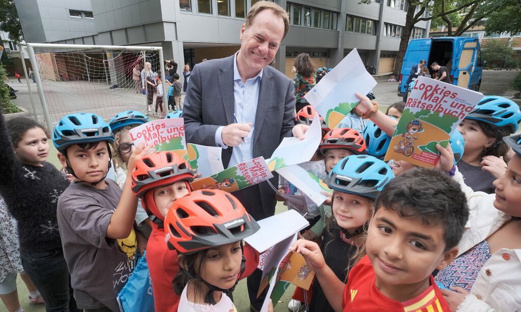 Oberbürgermeister Keller steht auf einem Schulhof und ist umringt von Grundschulkindern, die Malbücher in den Händen halten