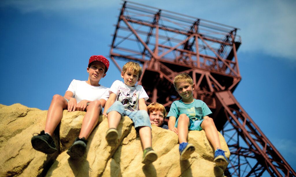 Vier Jungs sitzen auf einem Felsen, im Hintergrund ein Förderturm