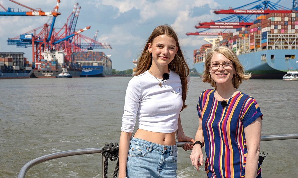 zwei Mädchen auf einem Schiff im Hamburger Hafen, im Hintergrund Hafenanlage und Containerschiff