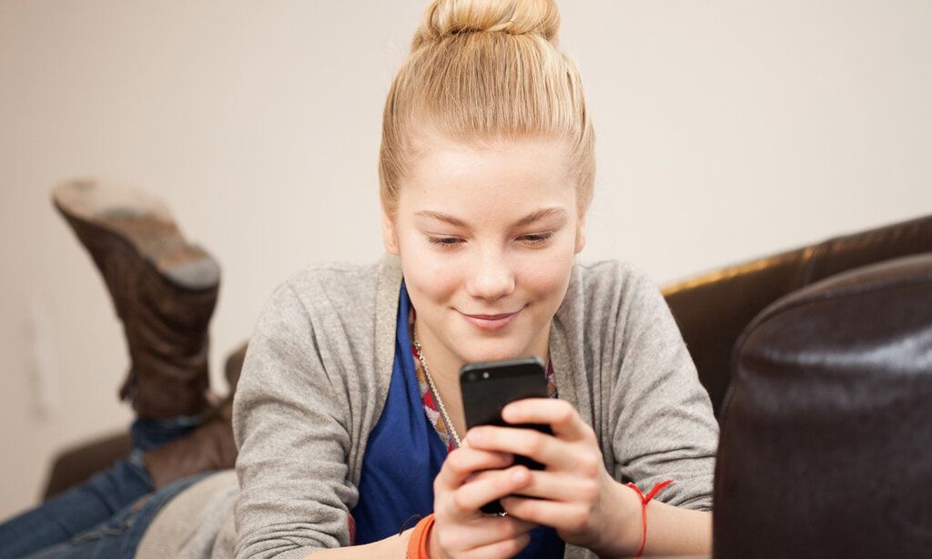 Mädchen liegt auf einer Couch und guckt aufs Smartphone