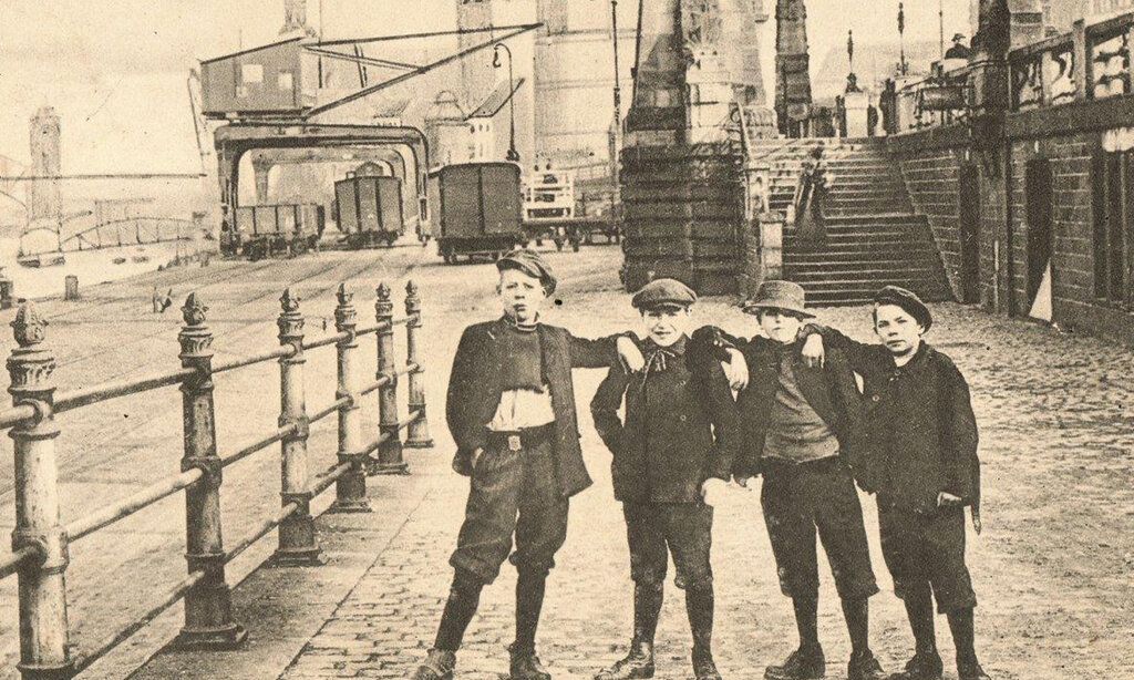 historisches Foto von 4 Jungen auf der unteren Rheinwerft; im Hintergrund Hafenbetrieb; Pegeluhr; Schlossturm