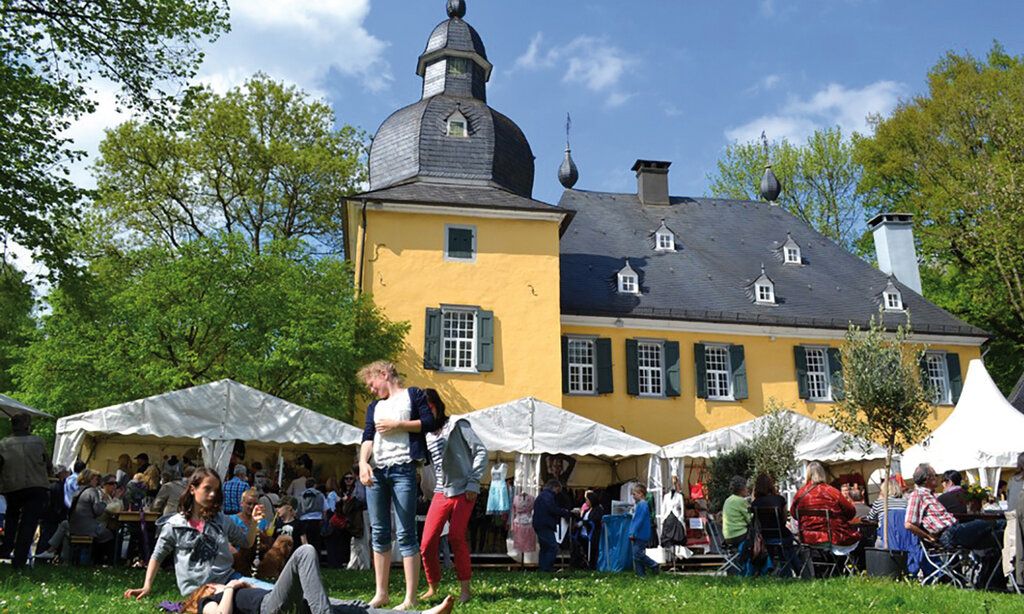 Außenansicht von Schloss Lüntenbeck, davor Pavillons und Leute