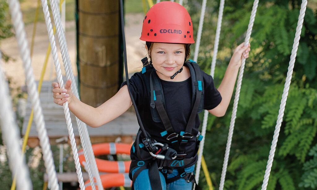 Mädchen mit Helm klettert im Hochseilgarten