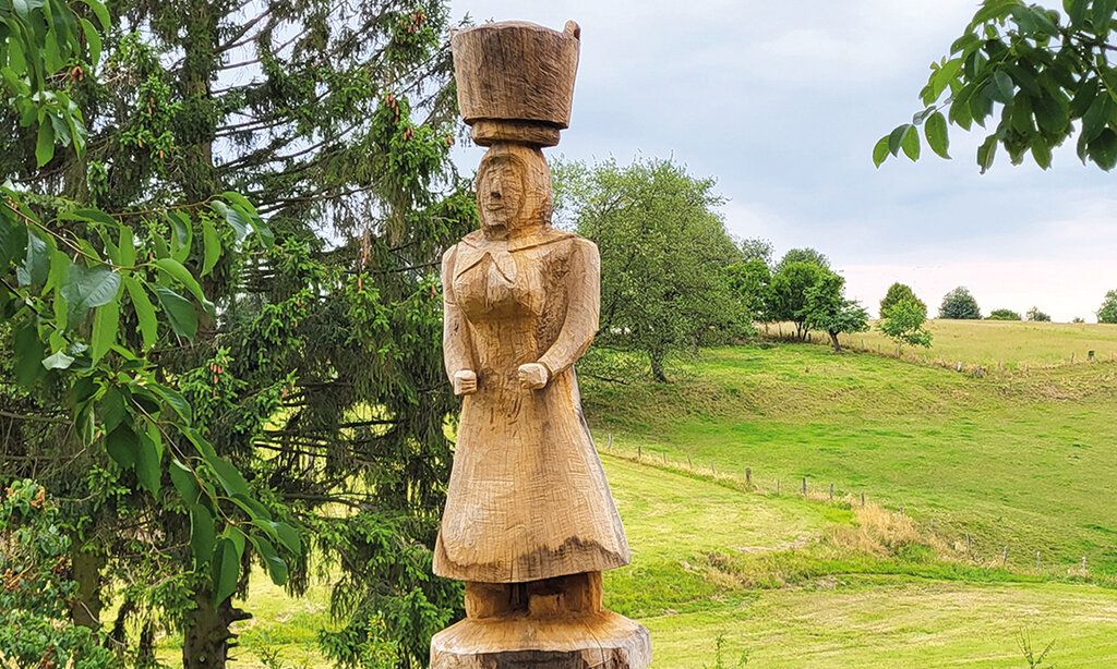 Holzskulptur einer Frau mit einem Korb auf dem Kopf in Landschaft