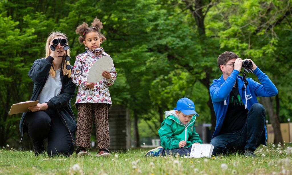 Vater, Mutter und zwei Kinder sind im Park und zählen Vögel