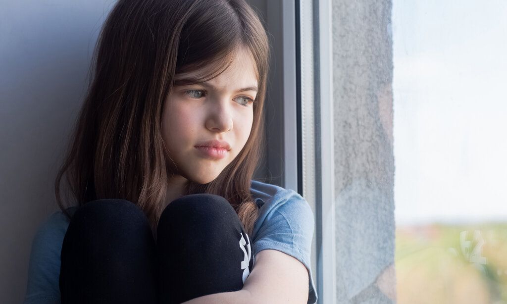 ein trauriges Mädchen sitzt am Fenster