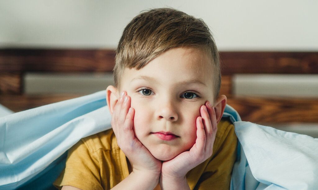 Junge liegt im Bett und guckt nicht fröhlich