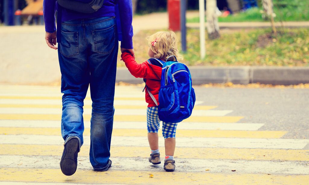 Vater und Kind überqueren Hand in Hand eine Straße, Sicht von hinten