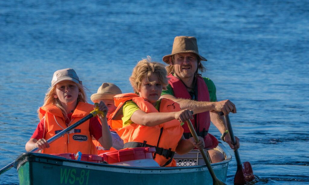 Vater paddelt mit Kindern im Paddelboot auf einem See